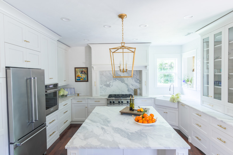 Transitional u-shaped dark wood floor and brown floor kitchen photo with a farmhouse sink, shaker cabinets, white cabinets, marble countertops, marble backsplash, stainless steel appliances and an island