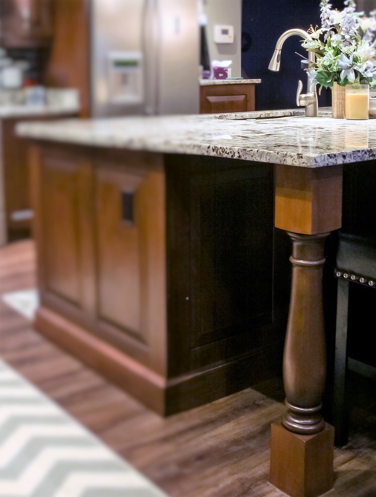 Large transitional l-shaped medium tone wood floor home design photo with an undermount sink, raised-panel cabinets, medium tone wood cabinets, granite countertops, glass tile backsplash, stainless steel appliances and an island
