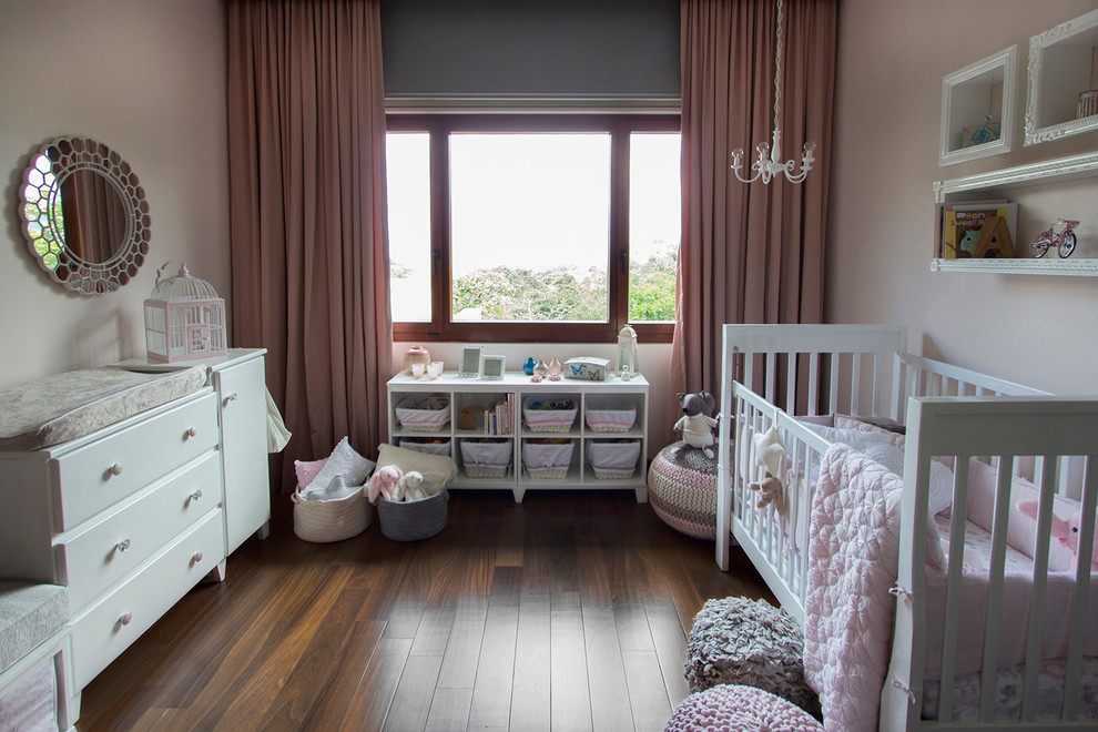 Small traditional nursery in Other with pink walls and medium hardwood floors for girls.