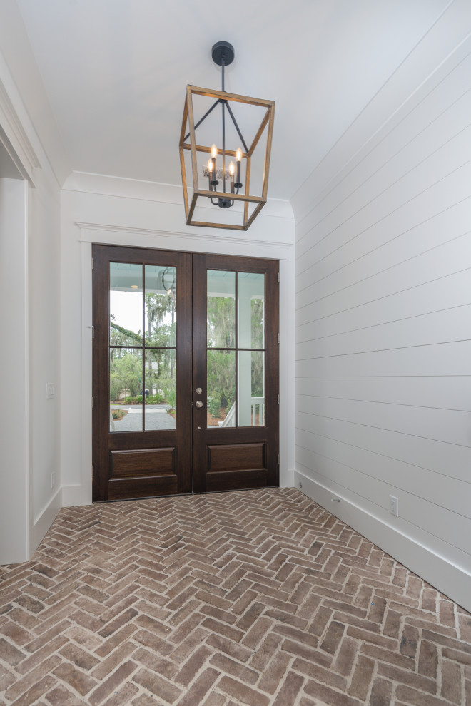 Immagine di un ingresso o corridoio stile marinaro con pareti bianche, pavimento in mattoni, una porta a due ante, una porta in legno scuro e pareti in perlinato