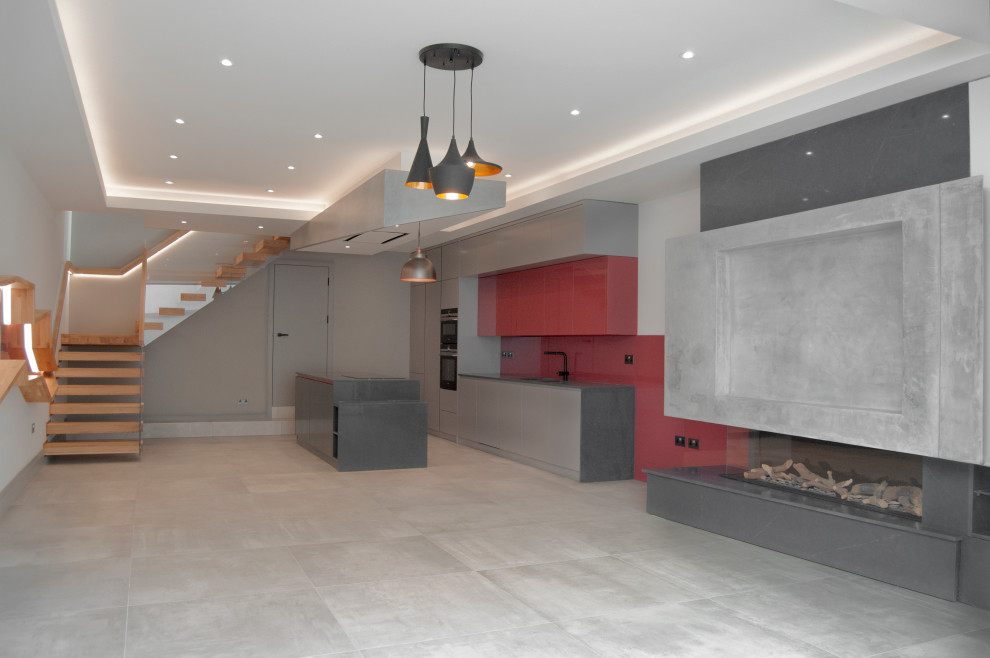 Photo of a large modern single-wall open plan kitchen in London with a double-bowl sink, flat-panel cabinets, grey cabinets, quartzite benchtops, red splashback, glass sheet splashback, black appliances, cement tiles, with island, grey floor and grey benchtop.