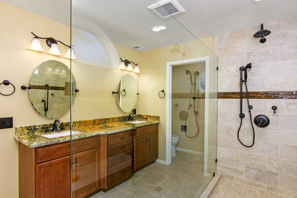 This is an example of a large traditional master bathroom in San Diego with recessed-panel cabinets, medium wood cabinets, a curbless shower, a two-piece toilet, beige tile, ceramic tile, beige walls, travertine floors, granite benchtops, an undermount sink, an open shower, beige benchtops, a double vanity and a built-in vanity.