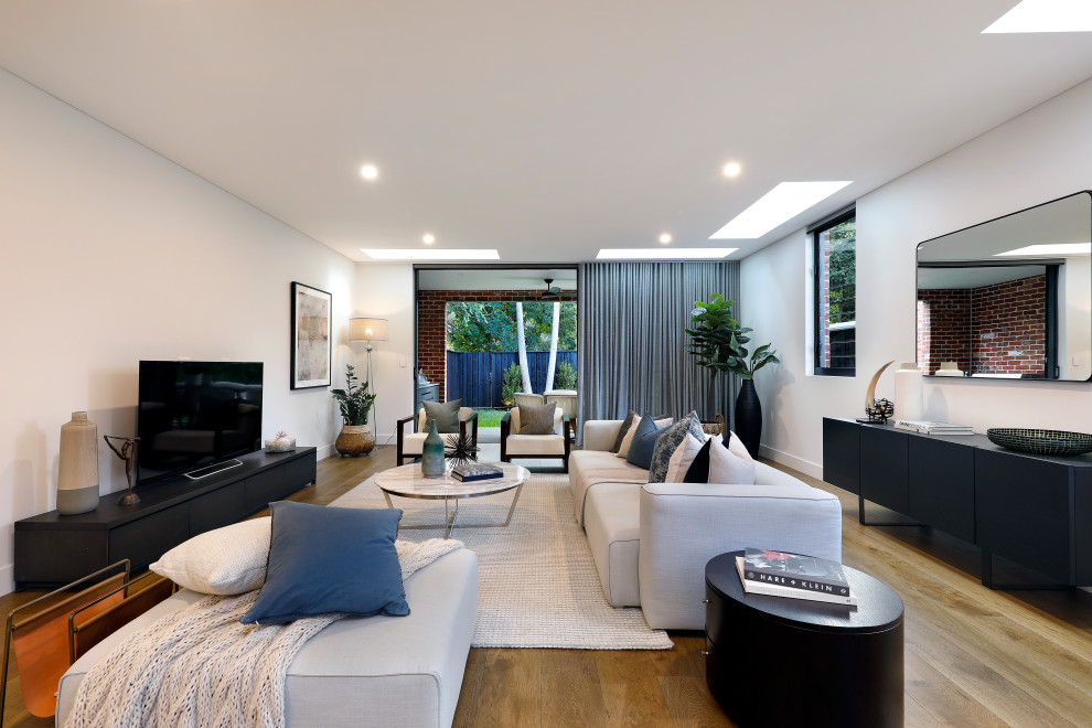 This is an example of a mid-sized contemporary open concept living room in Sydney with white walls, a freestanding tv, medium hardwood floors and brown floor.