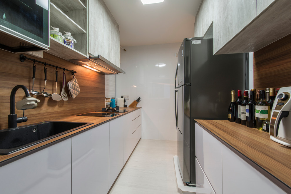 This is an example of a scandinavian galley kitchen in Singapore with a drop-in sink, flat-panel cabinets, white cabinets, wood benchtops, brown splashback, black appliances, light hardwood floors and no island.