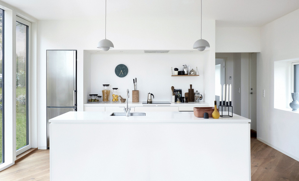This is an example of a mid-sized scandinavian galley separate kitchen in Copenhagen with an undermount sink, flat-panel cabinets, white cabinets, stainless steel appliances, medium hardwood floors, with island and laminate benchtops.