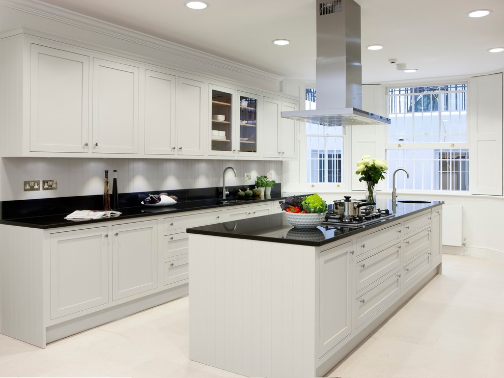 Photo of a mid-sized traditional galley separate kitchen in London with an integrated sink, shaker cabinets, white cabinets, white splashback, stainless steel appliances, with island, solid surface benchtops, white floor and black benchtop.