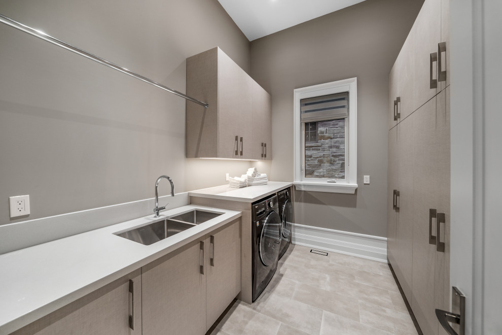 Large galley laundry room in Toronto with a double-bowl sink, flat-panel cabinets, granite benchtops, grey walls, a side-by-side washer and dryer and white benchtop.