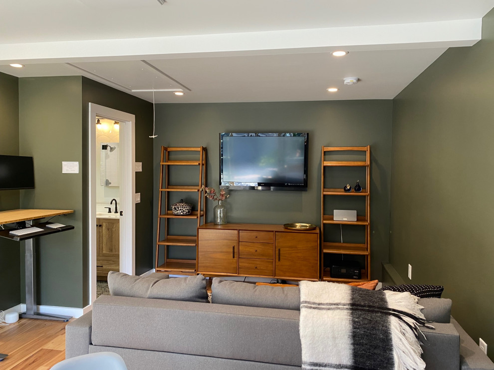 Modelo de sala de estar abierta clásica renovada pequeña con paredes verdes, suelo de madera clara, televisor colgado en la pared y suelo beige