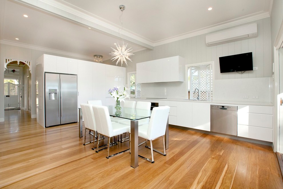 Design ideas for an expansive contemporary l-shaped eat-in kitchen in Brisbane with a double-bowl sink, flat-panel cabinets, white cabinets, solid surface benchtops, white splashback, glass sheet splashback, stainless steel appliances, light hardwood floors and no island.