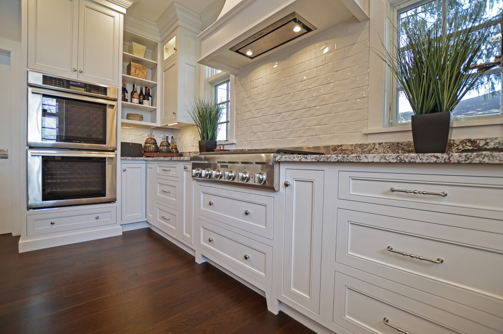 Eat-in kitchen - transitional dark wood floor and brown floor eat-in kitchen idea with an undermount sink, shaker cabinets, white cabinets, granite countertops, white backsplash, ceramic backsplash, stainless steel appliances, an island and beige countertops