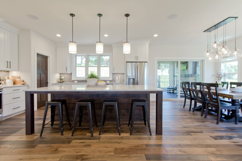 Transitional l-shaped medium tone wood floor and brown floor eat-in kitchen photo with recessed-panel cabinets, dark wood cabinets, quartz countertops, gray backsplash, mosaic tile backsplash, stainless steel appliances, an island and white countertops