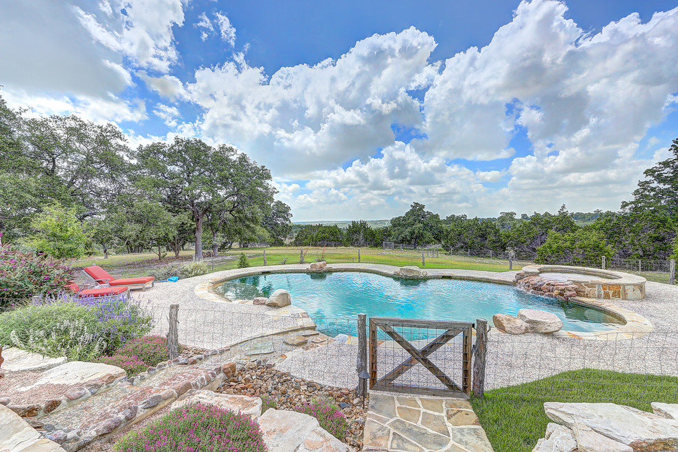 Large country backyard kidney-shaped natural pool in Austin with a hot tub and natural stone pavers.