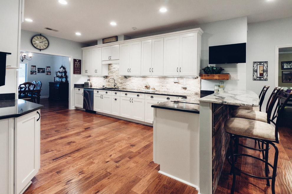 Large transitional galley light wood floor and brown floor open concept kitchen photo with an undermount sink, shaker cabinets, white cabinets, quartz countertops, white backsplash, stone tile backsplash, stainless steel appliances and a peninsula