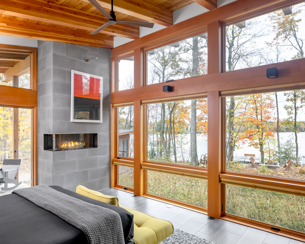 Inspiration for a mid-sized country master bedroom in Minneapolis with multi-coloured walls, porcelain floors, a two-sided fireplace, a concrete fireplace surround, grey floor, exposed beam and wood walls.