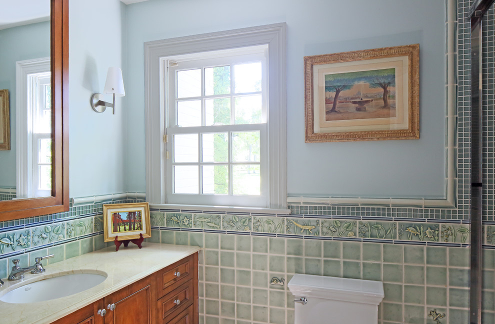 Design ideas for a mid-sized traditional kids bathroom in New York with recessed-panel cabinets, medium wood cabinets, an alcove tub, a shower/bathtub combo, a two-piece toilet, green tile, ceramic tile, blue walls, marble floors, an undermount sink and limestone benchtops.