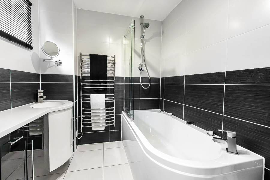 Inspiration for a medium sized contemporary bathroom in Essex with flat-panel cabinets, black cabinets, a freestanding bath, black and white tiles, ceramic tiles, porcelain flooring, an integrated sink, solid surface worktops, white floors, a sliding door and white worktops.