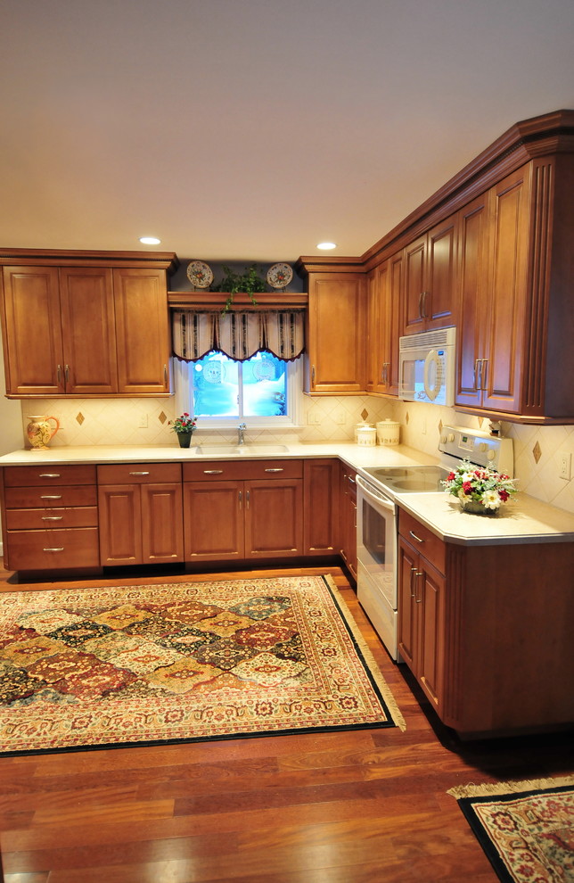 Inspiration for a mid-sized transitional medium tone wood floor eat-in kitchen remodel in New York with raised-panel cabinets, medium tone wood cabinets, solid surface countertops, ceramic backsplash, white appliances, no island, an undermount sink and beige backsplash