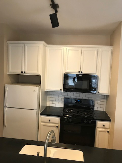 Inspiration for a mid-sized contemporary galley medium tone wood floor kitchen remodel in St Louis with an integrated sink, recessed-panel cabinets, white cabinets, solid surface countertops, white backsplash, subway tile backsplash, black appliances and black countertops