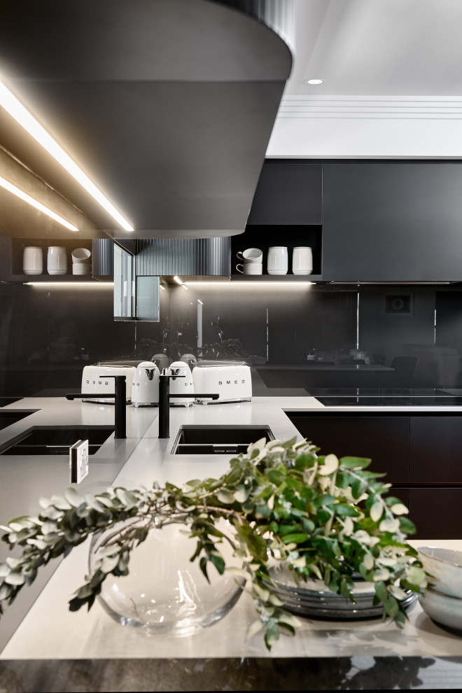 Inredning av ett modernt stort grå grått kök, med en undermonterad diskho, släta luckor, svarta skåp, bänkskiva i kvarts, svart stänkskydd, glaspanel som stänkskydd, svarta vitvaror, ljust trägolv, en köksö och brunt golv