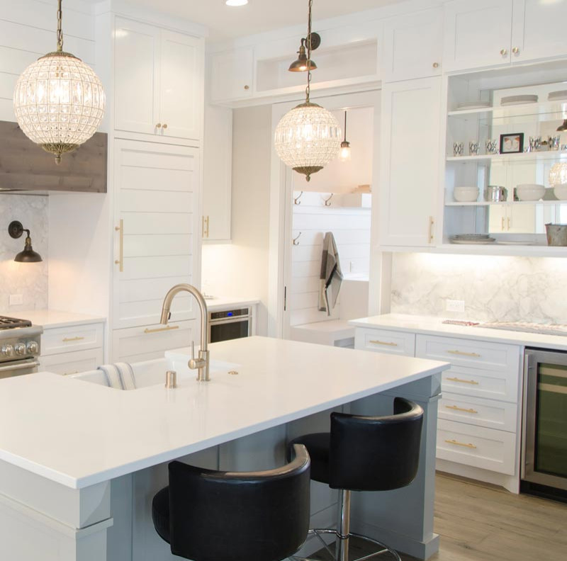 This is an example of a mid-sized contemporary l-shaped open plan kitchen in Orange County with shaker cabinets, white cabinets, quartzite benchtops, white splashback, with island, white benchtop, a farmhouse sink, marble splashback, stainless steel appliances, medium hardwood floors and grey floor.