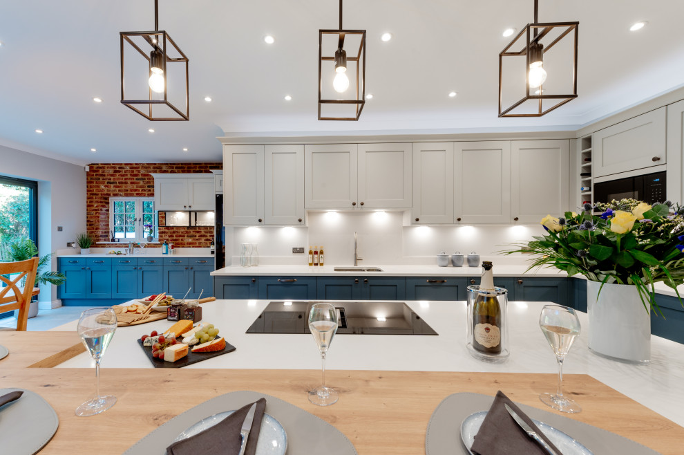 Design ideas for a large traditional l-shaped open plan kitchen in Surrey with an integrated sink, shaker cabinets, blue cabinets, quartz worktops, white splashback, engineered quartz splashback, integrated appliances, porcelain flooring, an island, grey floors, white worktops and a feature wall.