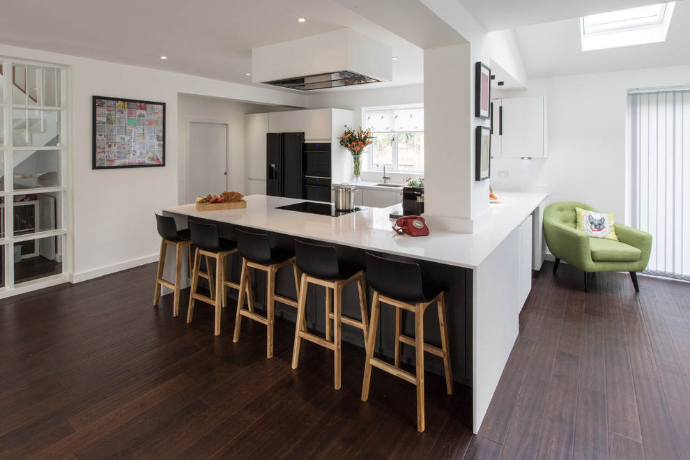 Photo of a mid-sized contemporary u-shaped open plan kitchen in London with an undermount sink, flat-panel cabinets, white cabinets, solid surface benchtops, black appliances, dark hardwood floors and a peninsula.