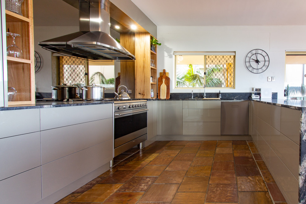 Inspiration for a large modern u-shaped kitchen pantry in Central Coast with a double-bowl sink, flat-panel cabinets, beige cabinets, granite benchtops, metallic splashback, glass sheet splashback, stainless steel appliances, slate floors, a peninsula, brown floor and black benchtop.