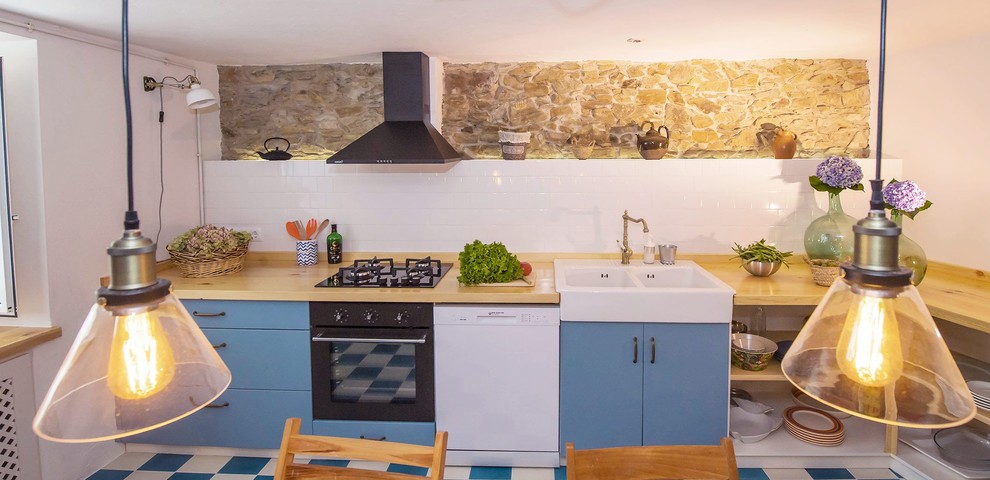 Mid-sized country l-shaped eat-in kitchen in Other with a double-bowl sink, glass-front cabinets, blue cabinets, wood benchtops, white splashback, ceramic splashback, black appliances, ceramic floors, no island and blue floor.