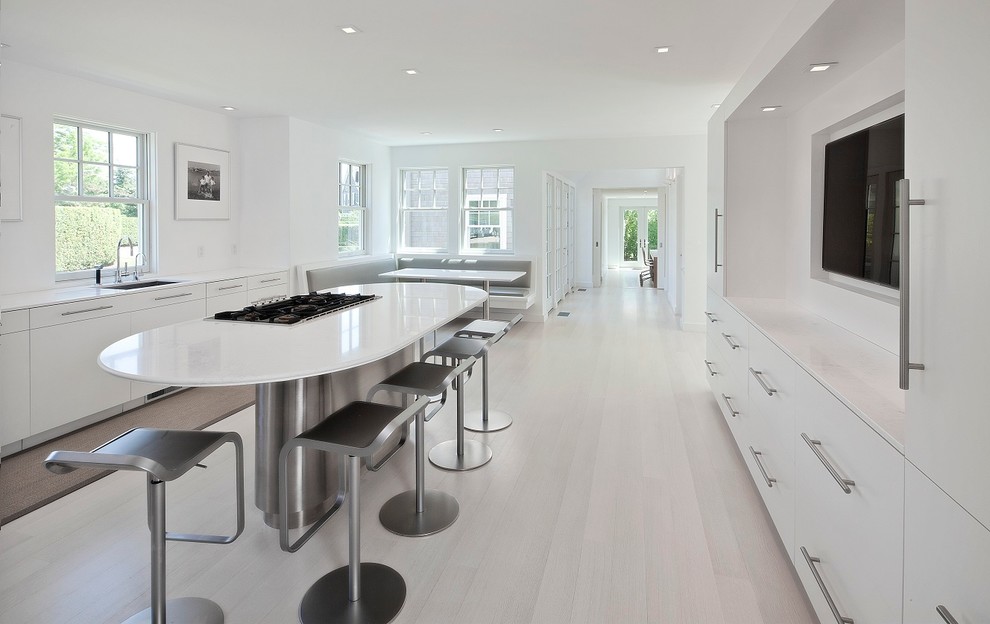 This is an example of a large modern single-wall eat-in kitchen in Cleveland with a drop-in sink, flat-panel cabinets, white cabinets, white splashback, stainless steel appliances, light hardwood floors and with island.