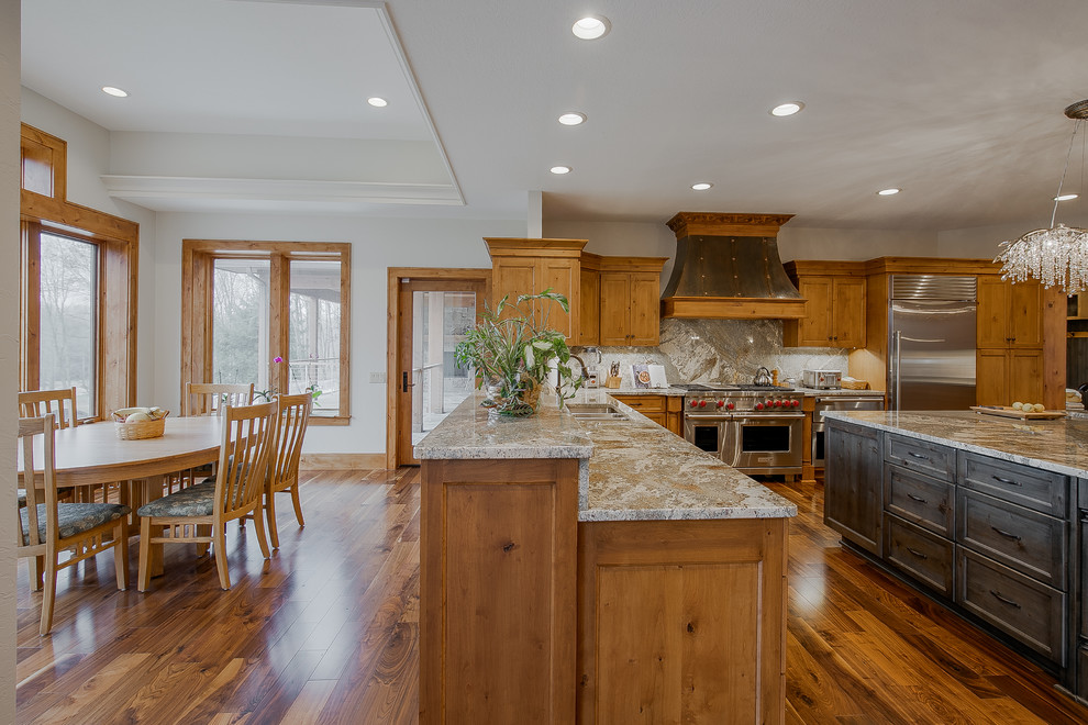 Photo of a large country u-shaped eat-in kitchen in Cleveland with a double-bowl sink, recessed-panel cabinets, medium wood cabinets, quartz benchtops, grey splashback, porcelain splashback, stainless steel appliances, medium hardwood floors, with island and grey benchtop.