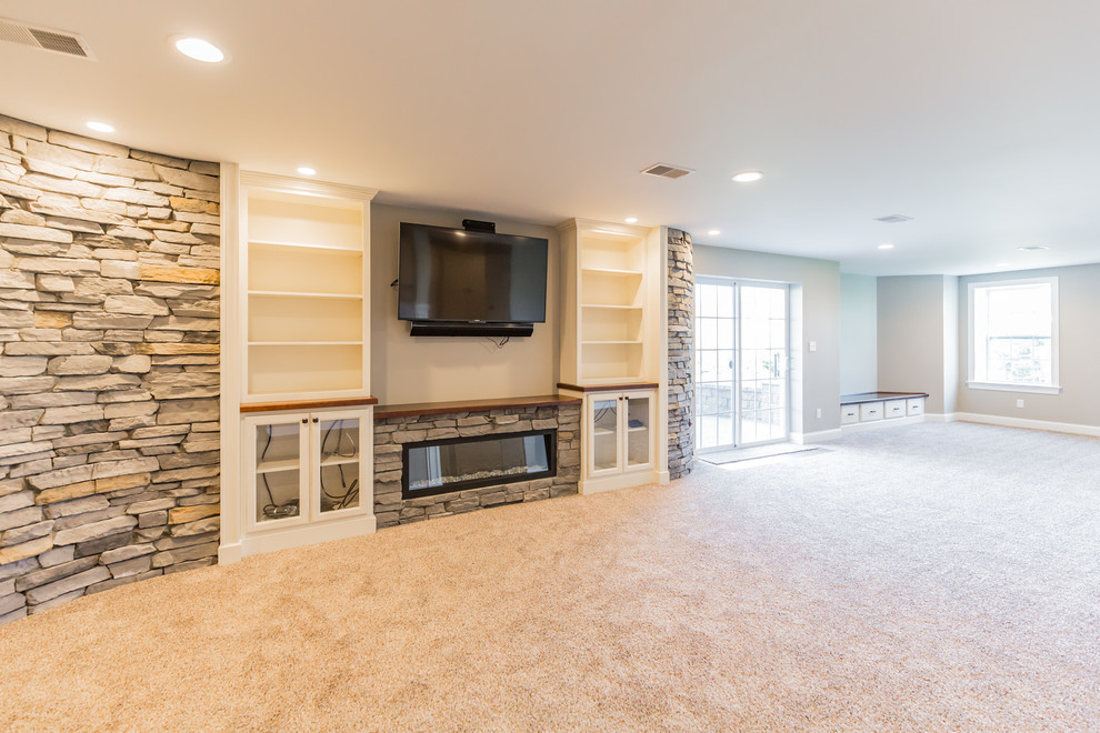 Photo of a large transitional walk-out basement in Philadelphia with beige walls, carpet, a ribbon fireplace, a stone fireplace surround and beige floor.