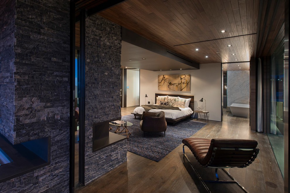 This is an example of a large modern master and grey and brown bedroom in Los Angeles with white walls, medium hardwood flooring, a standard fireplace, a stacked stone fireplace surround, brown floors and a drop ceiling.