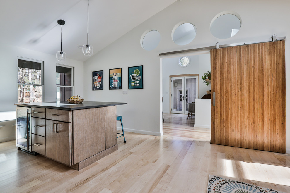 This is an example of a mid-sized contemporary l-shaped eat-in kitchen in Boston with an undermount sink, flat-panel cabinets, light wood cabinets, quartz benchtops, green splashback, porcelain splashback, stainless steel appliances, light hardwood floors, with island, beige floor and black benchtop.