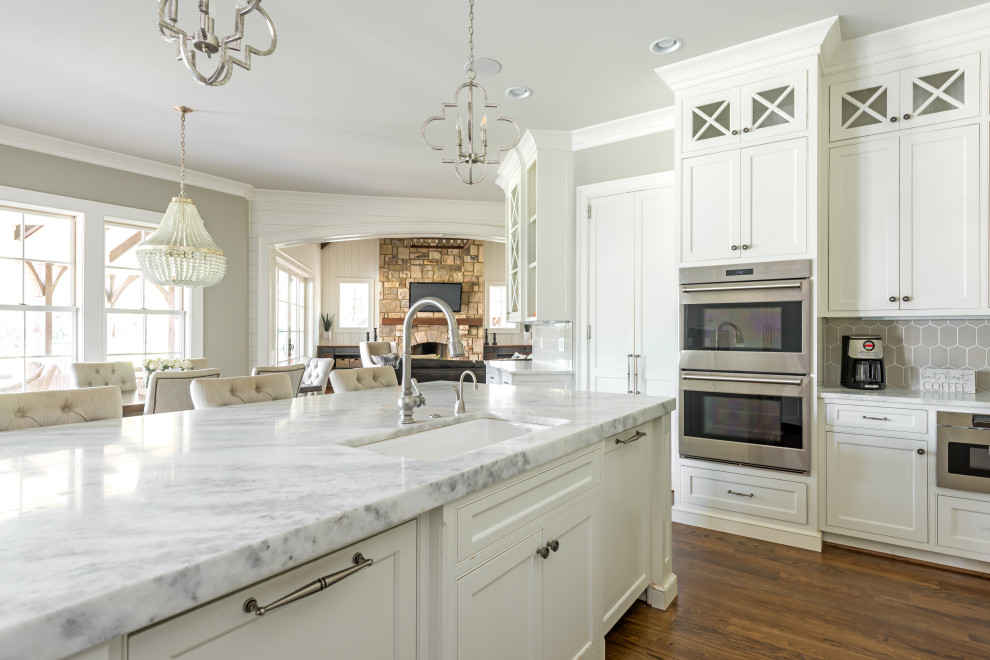 This is an example of a large traditional l-shaped kitchen in New York with a drop-in sink, quartzite benchtops, beige splashback, stainless steel appliances, dark hardwood floors, with island and white benchtop.