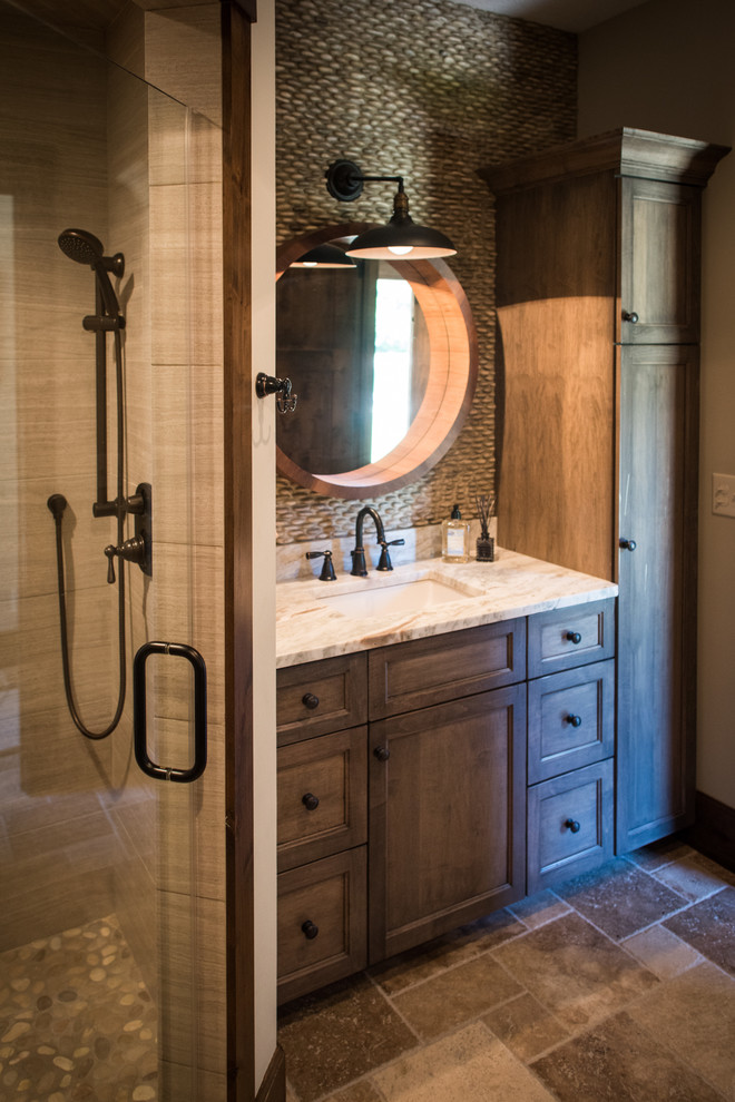 This is an example of a mid-sized country bathroom in Cleveland with dark wood cabinets, an alcove shower, beige tile, pebble tile, beige walls, travertine floors, an undermount sink and granite benchtops.