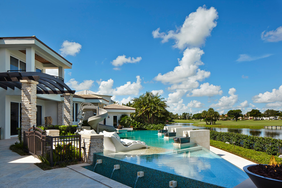 Design ideas for an expansive contemporary backyard custom-shaped infinity pool in Miami with a water slide and tile.