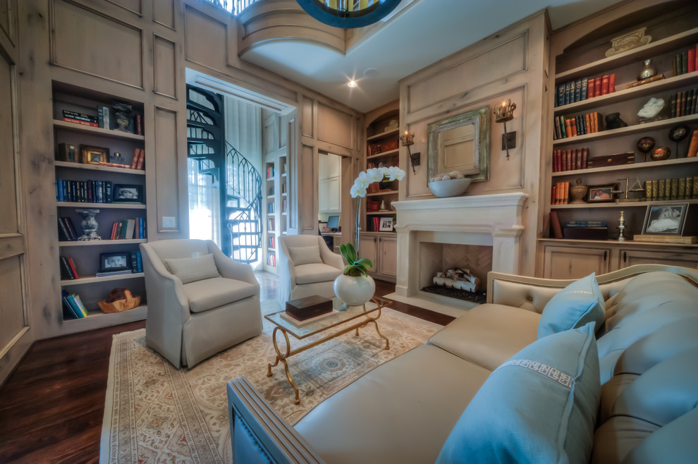 Photo of a large traditional home office in Houston with a library, beige walls, dark hardwood floors, a standard fireplace, a plaster fireplace surround and brown floor.