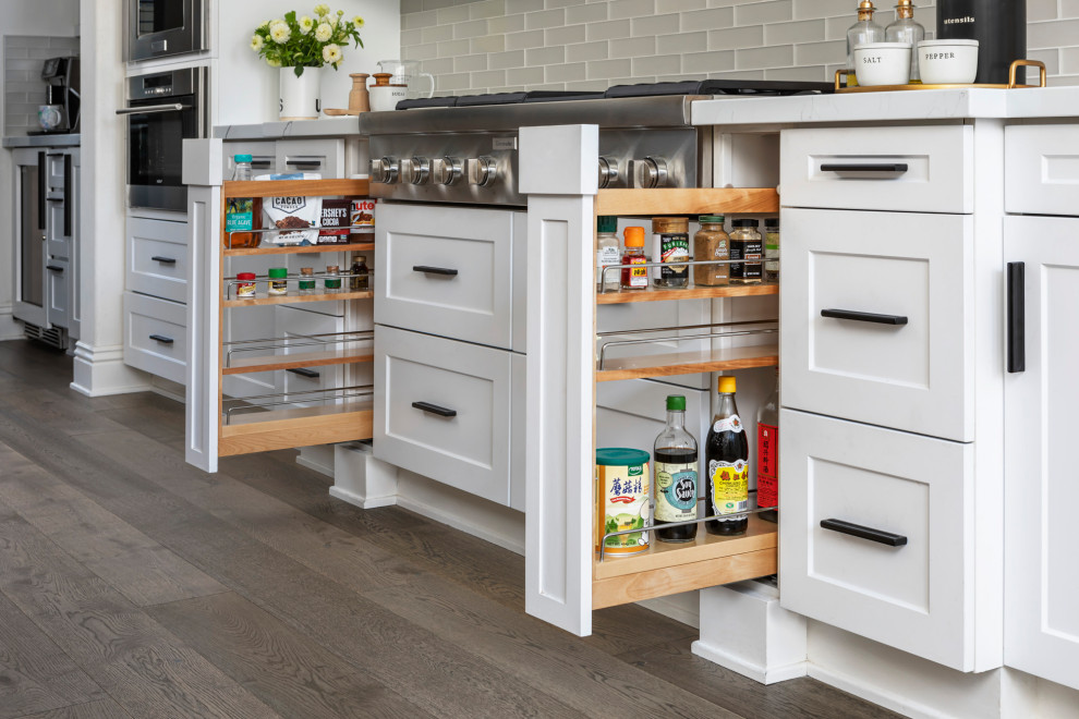 Example of a small minimalist galley dark wood floor and brown floor open concept kitchen design in Orange County with a farmhouse sink, shaker cabinets, white cabinets, quartzite countertops, white backsplash, glass tile backsplash, stainless steel appliances, an island and white countertops