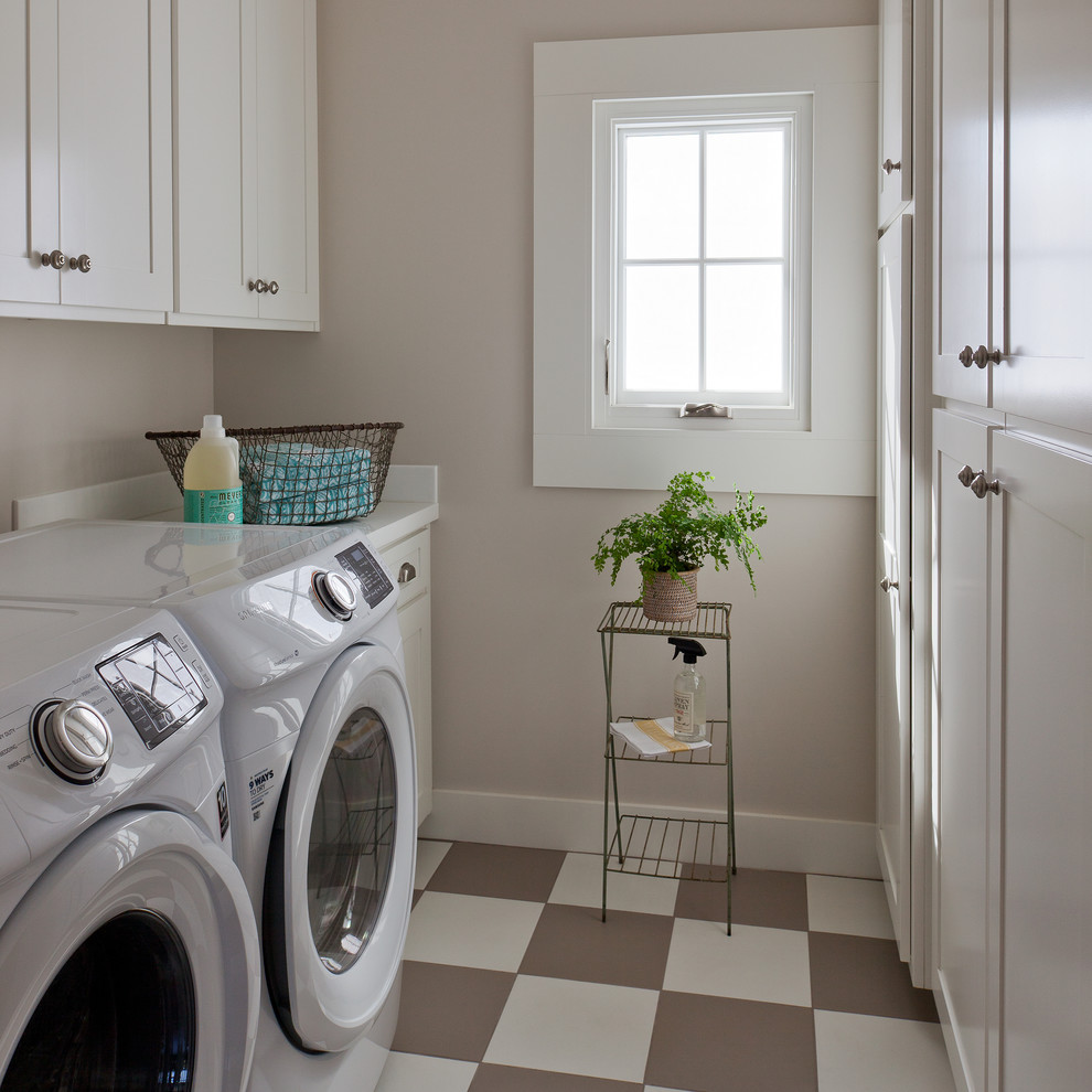 Photo of a country galley laundry room in Santa Barbara with shaker cabinets, white cabinets, beige walls, a side-by-side washer and dryer, multi-coloured floor and white benchtop.