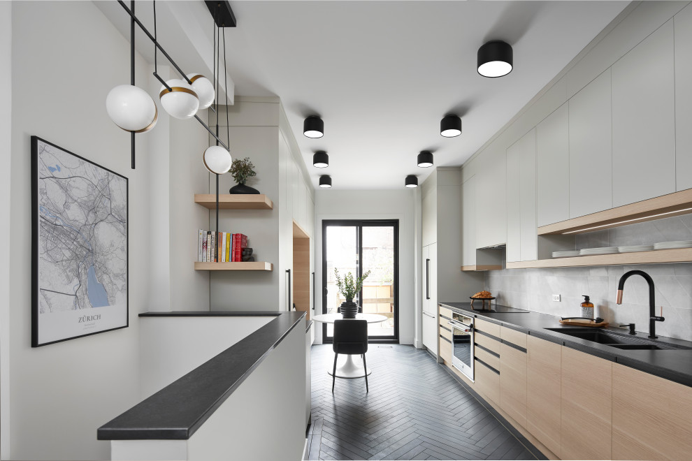 Mid-sized contemporary galley kitchen in Toronto with a double-bowl sink, flat-panel cabinets, light wood cabinets, quartz benchtops, grey splashback, porcelain splashback, stainless steel appliances, porcelain floors, no island, black floor and black benchtop.