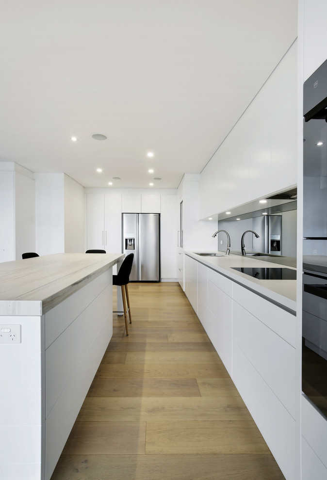Inspiration for a large modern l-shaped open plan kitchen in Sydney with an undermount sink, flat-panel cabinets, white cabinets, quartz benchtops, metallic splashback, mirror splashback, black appliances, light hardwood floors, with island and yellow floor.