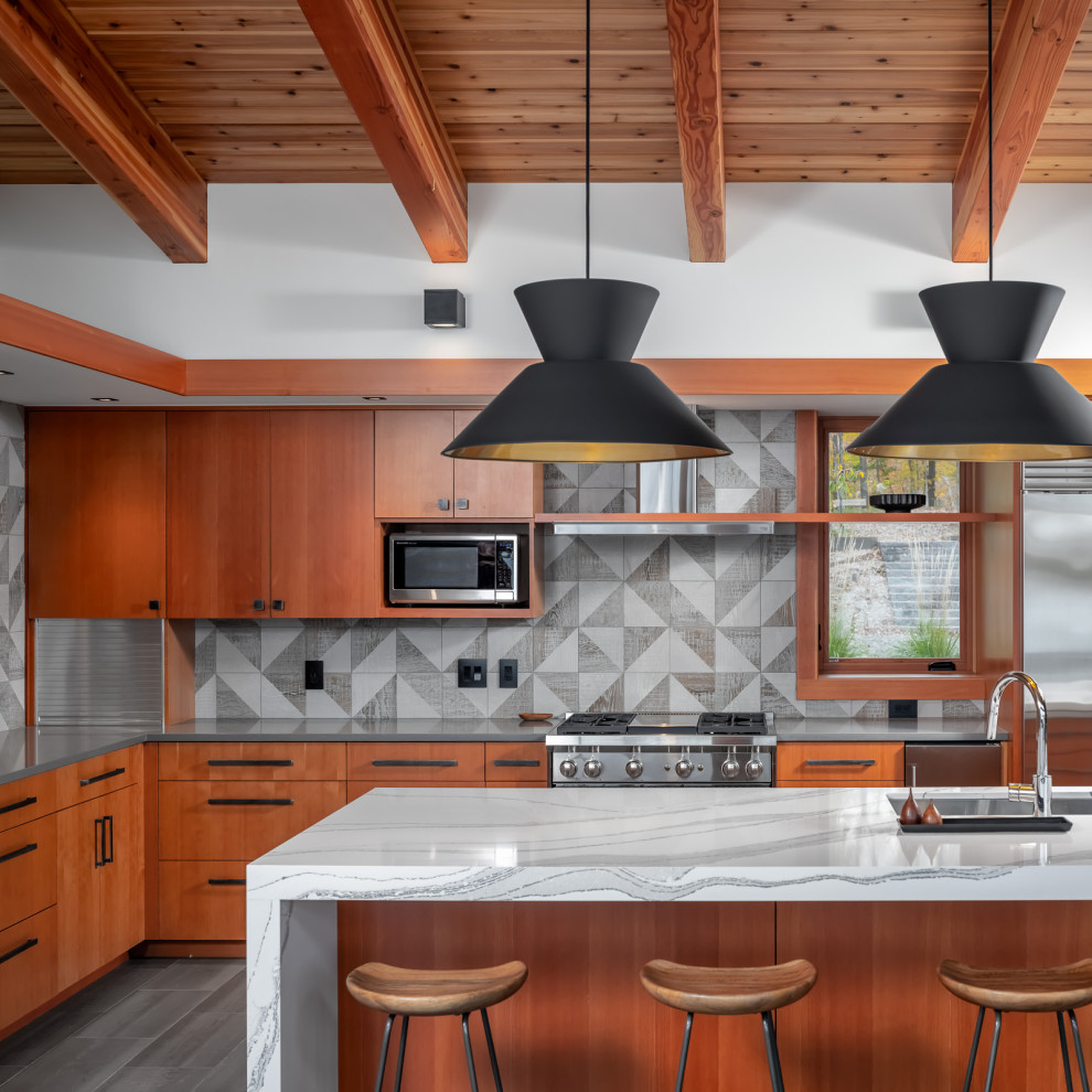 Foto på ett stort rustikt grå kök, med en undermonterad diskho, släta luckor, skåp i mellenmörkt trä, bänkskiva i kvarts, grått stänkskydd, stänkskydd i porslinskakel, rostfria vitvaror, klinkergolv i porslin, en köksö och grått golv