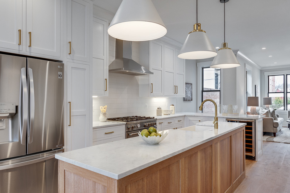 Transitional l-shaped medium tone wood floor and brown floor open concept kitchen photo in DC Metro with a farmhouse sink, shaker cabinets, white cabinets, white backsplash, subway tile backsplash, stainless steel appliances, an island and white countertops