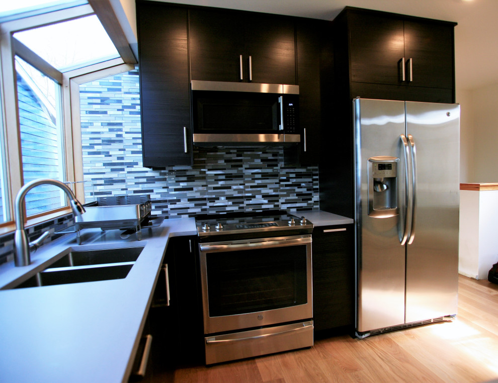 Photo of a small contemporary u-shaped kitchen in Seattle with a double-bowl sink, flat-panel cabinets, black cabinets, solid surface benchtops, blue splashback, matchstick tile splashback, stainless steel appliances, light hardwood floors, a peninsula, beige floor and grey benchtop.