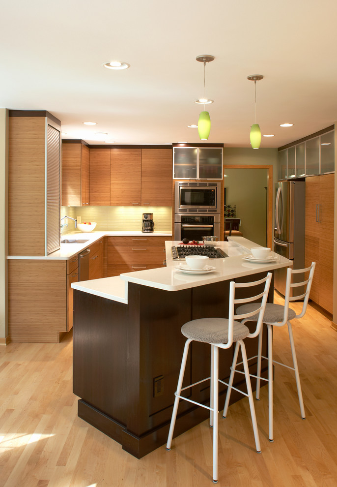 This is an example of a contemporary l-shaped eat-in kitchen in Milwaukee with an undermount sink, flat-panel cabinets, medium wood cabinets, glass tile splashback and stainless steel appliances.