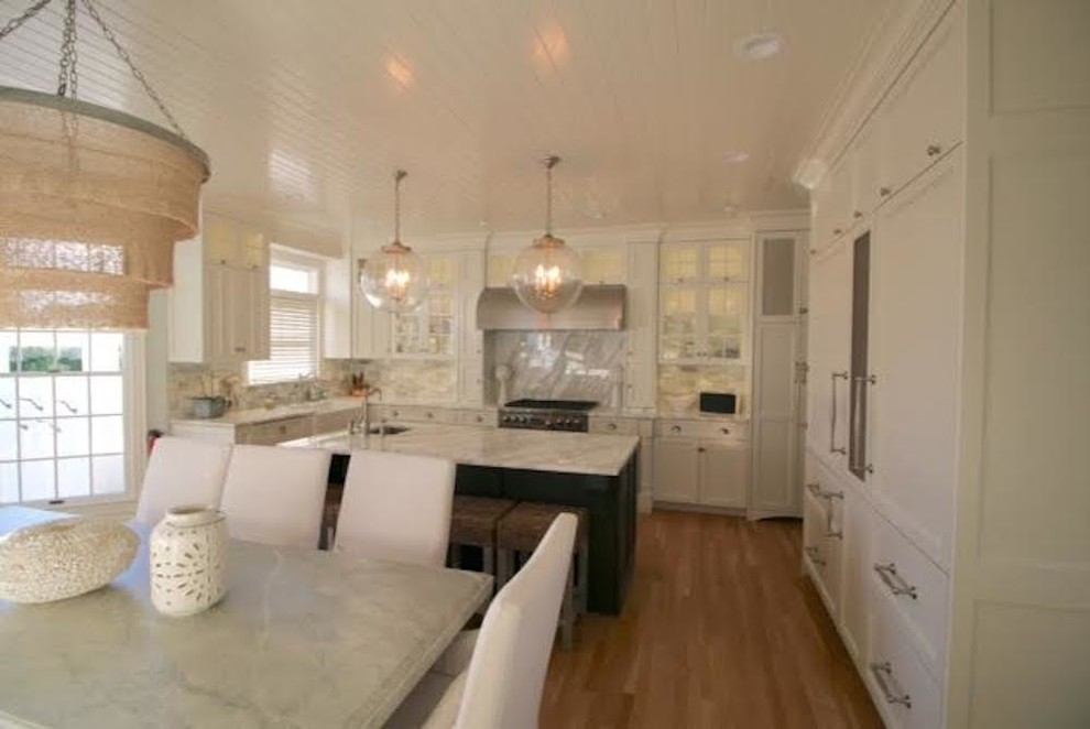 Photo of a large modern u-shaped eat-in kitchen in New York with a farmhouse sink, shaker cabinets, white cabinets, marble benchtops, grey splashback, marble splashback, white appliances, medium hardwood floors, with island and brown floor.