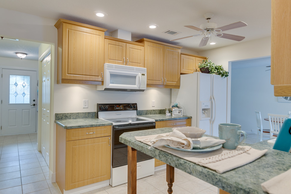 This is an example of a small tropical galley separate kitchen in Orlando with a double-bowl sink, raised-panel cabinets, medium wood cabinets, laminate benchtops, green splashback, white appliances, ceramic floors, no island and white floor.