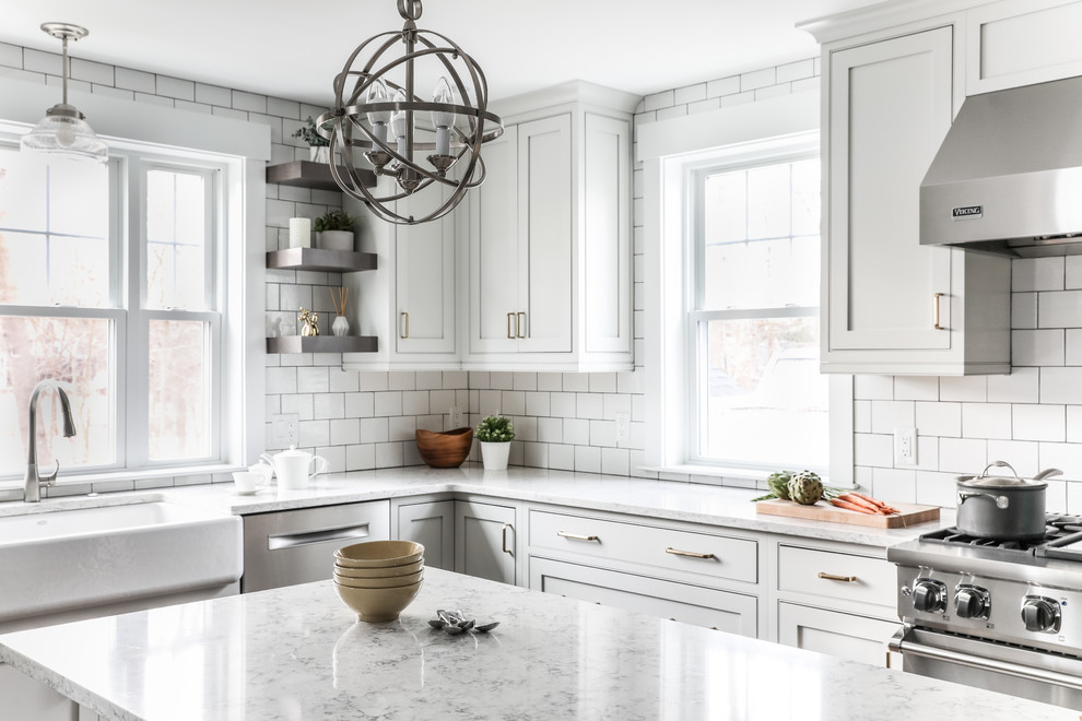 This is an example of a transitional l-shaped eat-in kitchen in Boston with a farmhouse sink, beaded inset cabinets, white cabinets, quartz benchtops, white splashback, subway tile splashback, stainless steel appliances, medium hardwood floors, with island, brown floor and grey benchtop.