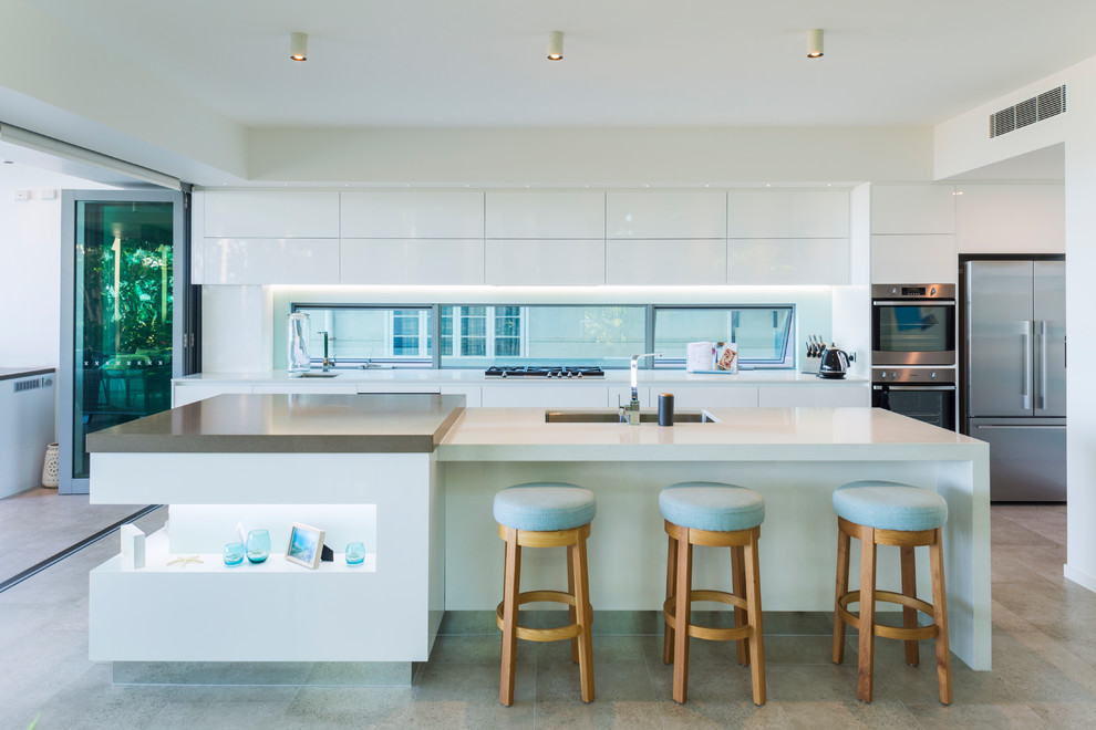 Photo of an expansive contemporary kitchen in Cairns with white cabinets, solid surface benchtops, stainless steel appliances, porcelain floors, with island, grey floor, white benchtop, an undermount sink, flat-panel cabinets and window splashback.