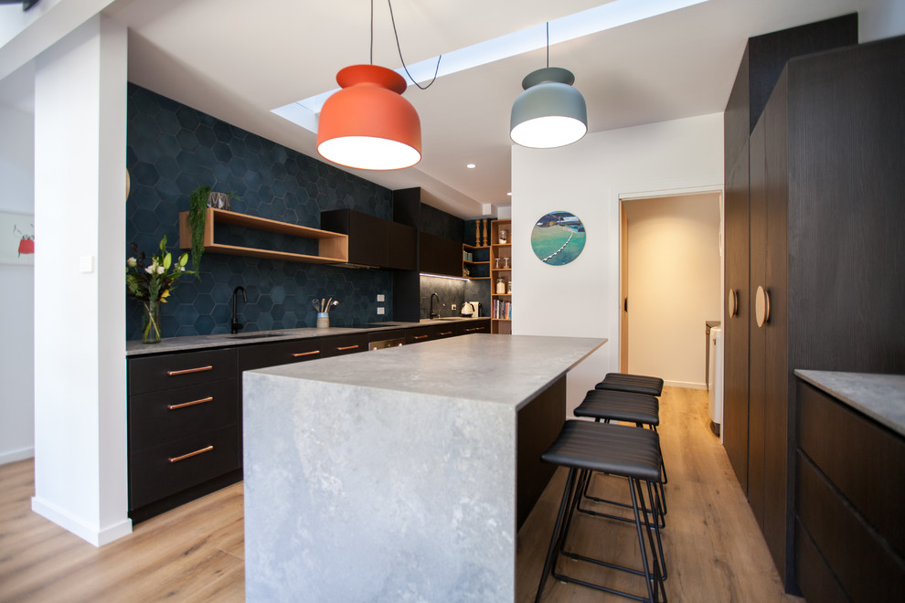 Mid-sized contemporary u-shaped eat-in kitchen in Hobart with black cabinets, solid surface benchtops, blue splashback, stainless steel appliances, light hardwood floors, with island and an undermount sink.